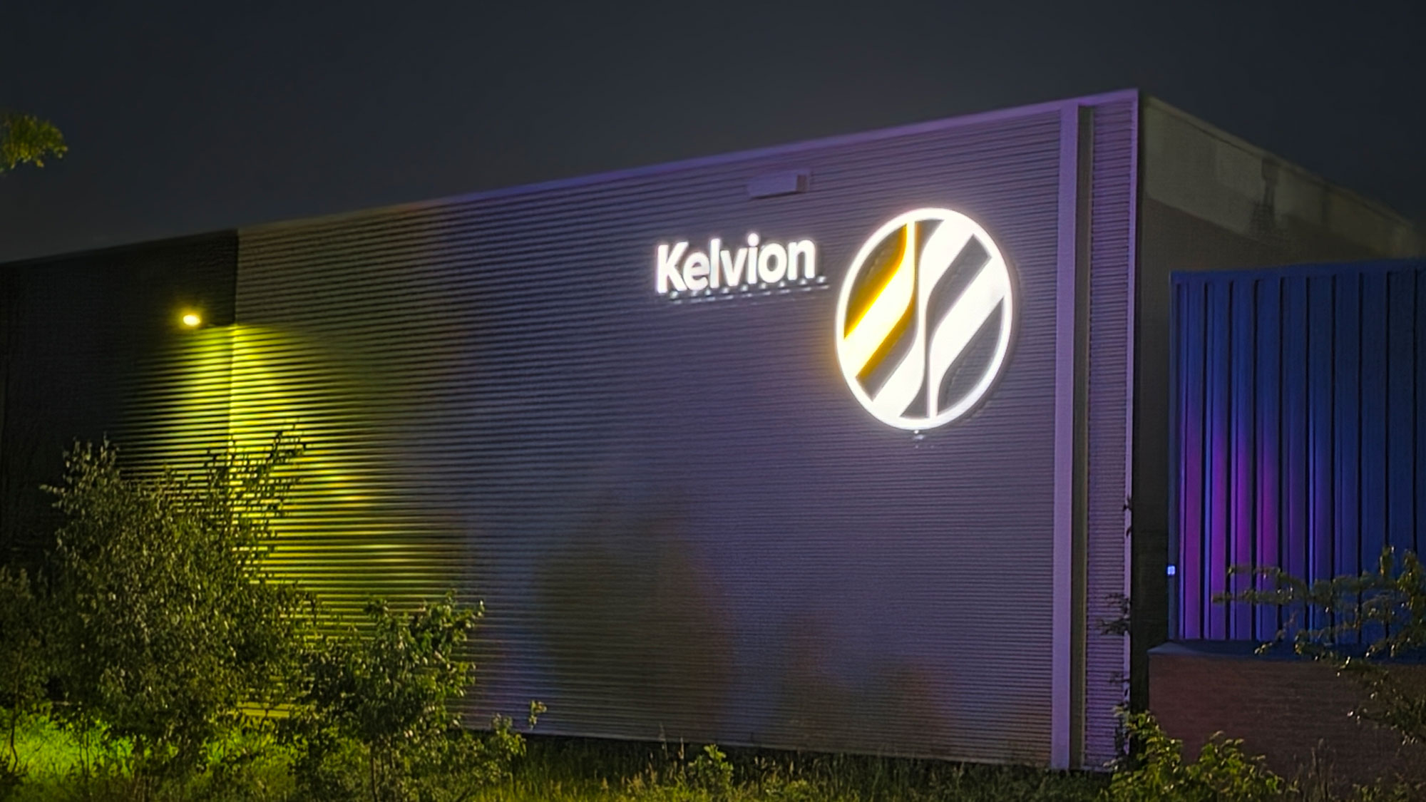 Kelvion-gevellogo verlicht tijdens het blauwe uur tegen een diepblauwe avondlucht Kelvion-gevellogo verlicht tijdens het blauwe uur tegen een diepblauwe avondlucht