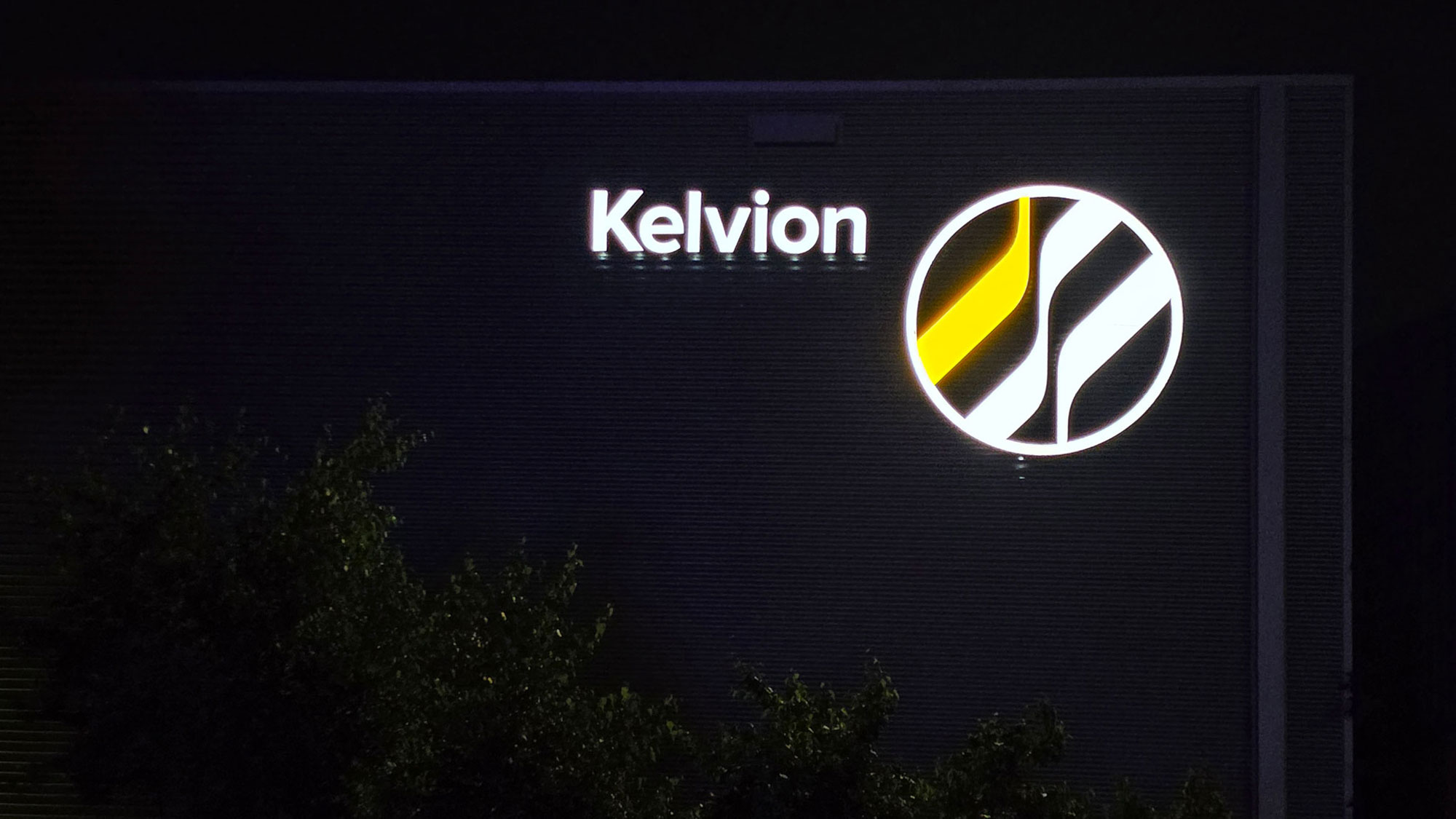 Verlicht Kelvion-gevellogo dat ’s avonds helder wit oplicht door 3M Day & Night-folie Verlicht Kelvion-gevellogo dat 's avonds helder wit oplicht door 3M Day & Night-folie