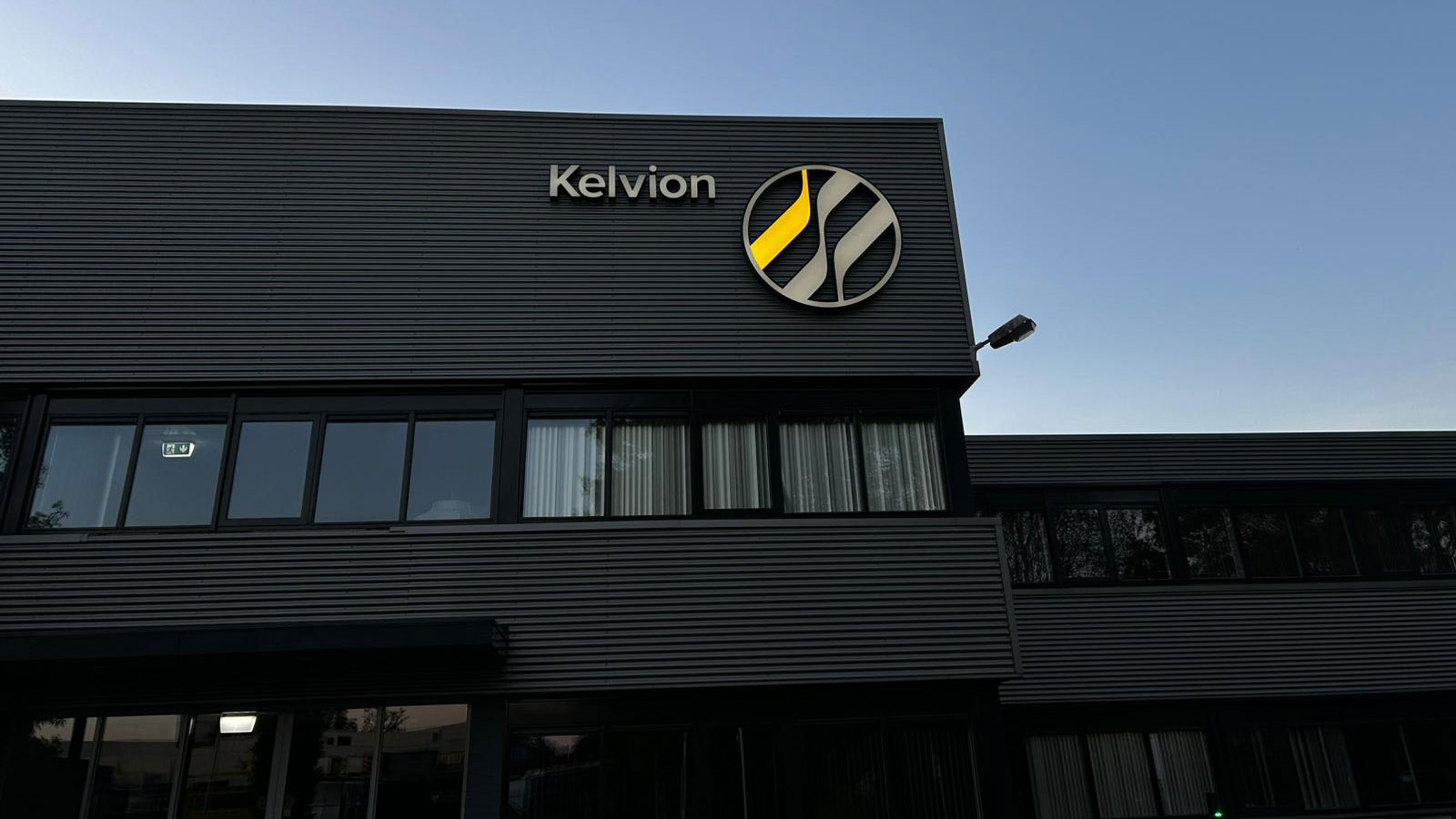 Verlicht Kelvion-gevellogo op het kantoorpand tijdens het blauwe uur Verlicht Kelvion-gevellogo op het kantoorpand tijdens het blauwe uur